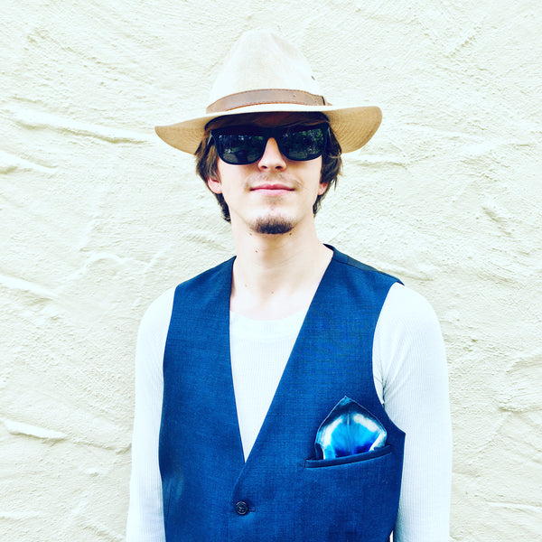Model is wearing a blue and white geometric patterned luxury silk pocket square handkerchief in his pocket.  This is a hand dyed, one of a kind, sustainable wear pocket square with many style looks. Best fashion accessory for any season or occasion. Makes a great gift. Handmade one of a kind artisan accessories. Square shaped 11 inches by 11 inches.