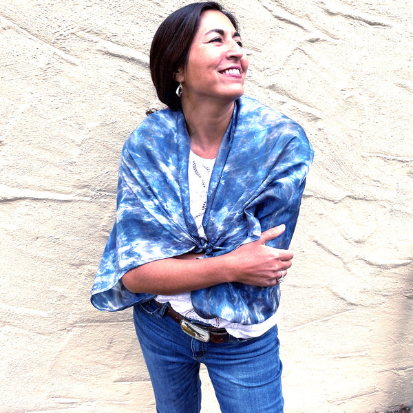 Model is wearing a blue luxury large silk square shawl wrapped around her shoulders in tie dye shibori pattern, sustainable wear with many style looks. Best fashion accessory for any season or occasion. Makes a great gift. Handmade one of a kind artisan accessories. Square shaped 43 inches by 43 inches.