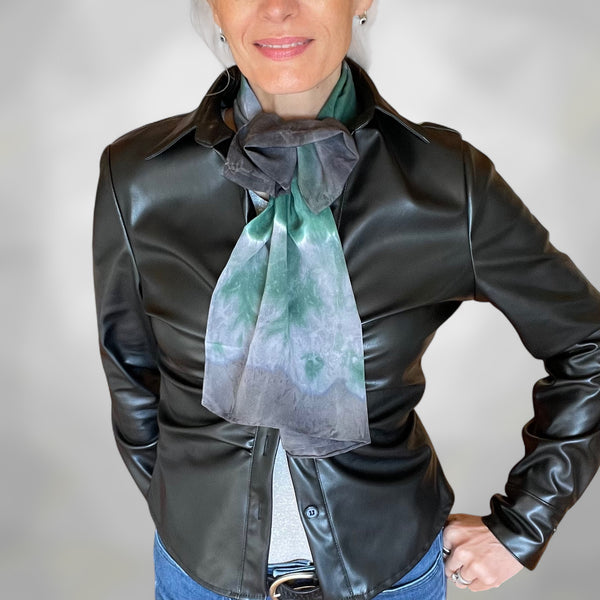 Person wearing a black leather jacket with a green and gray scarf around their neck on a plain background
