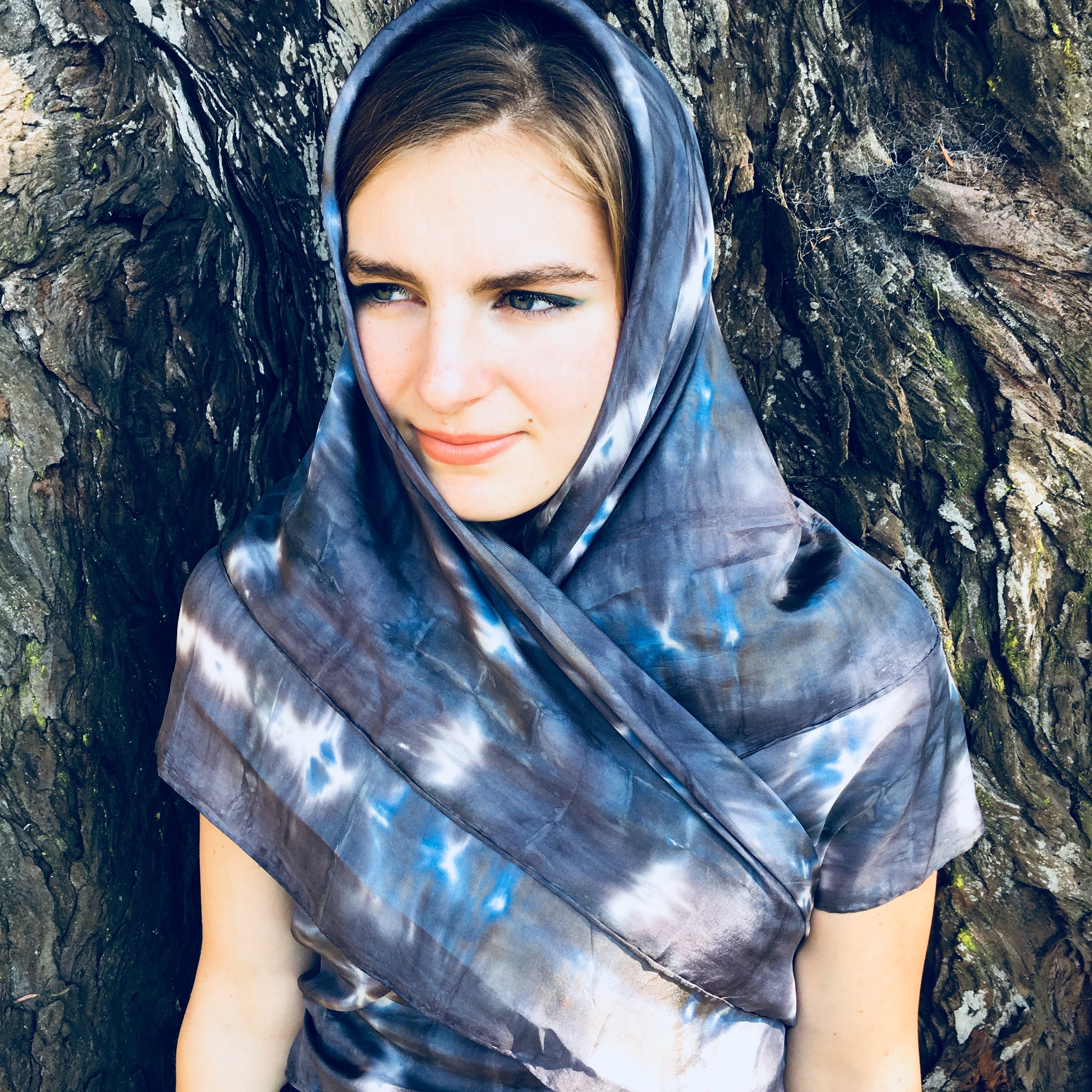 Model is wearing a black charcoal and blue large luxury silk square scarf as a hijab around head, sustainable wear with many style looks. Best fashion accessory for any season or occasion. Makes a great gift. Handmade one of a kind artisan accessories. Square shaped 43 inches by 43 inches.