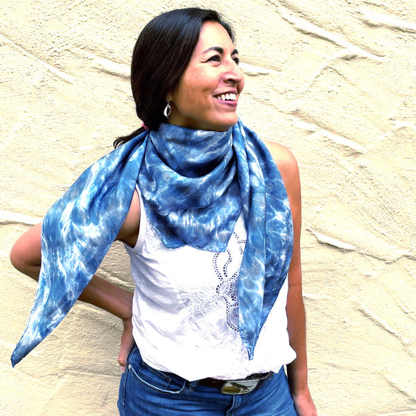 Model is wearing a blue luxury large silk square scarf shawl around her neck in tie dye shibori pattern, sustainable wear with many style looks. Best fashion accessory for any season or occasion. Makes a great gift. Handmade one of a kind artisan accessories. Square shaped 43 inches by 43 inches.
