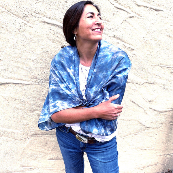 Model is wearing a blue luxury large silk square shawl wrapped around her shoulders in tie dye shibori pattern, sustainable wear with many style looks. Best fashion accessory for any season or occasion. Makes a great gift. Handmade one of a kind artisan accessories. Square shaped 43 inches by 43 inches.